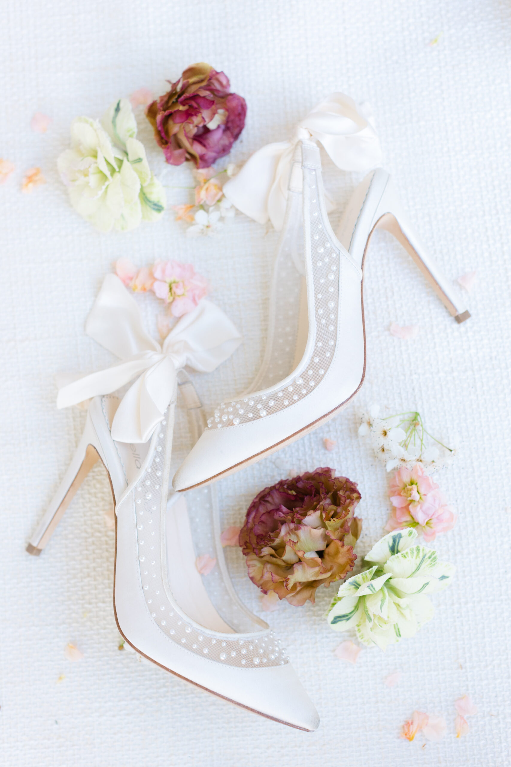 white wedding shoes lying on a mat next to flowers